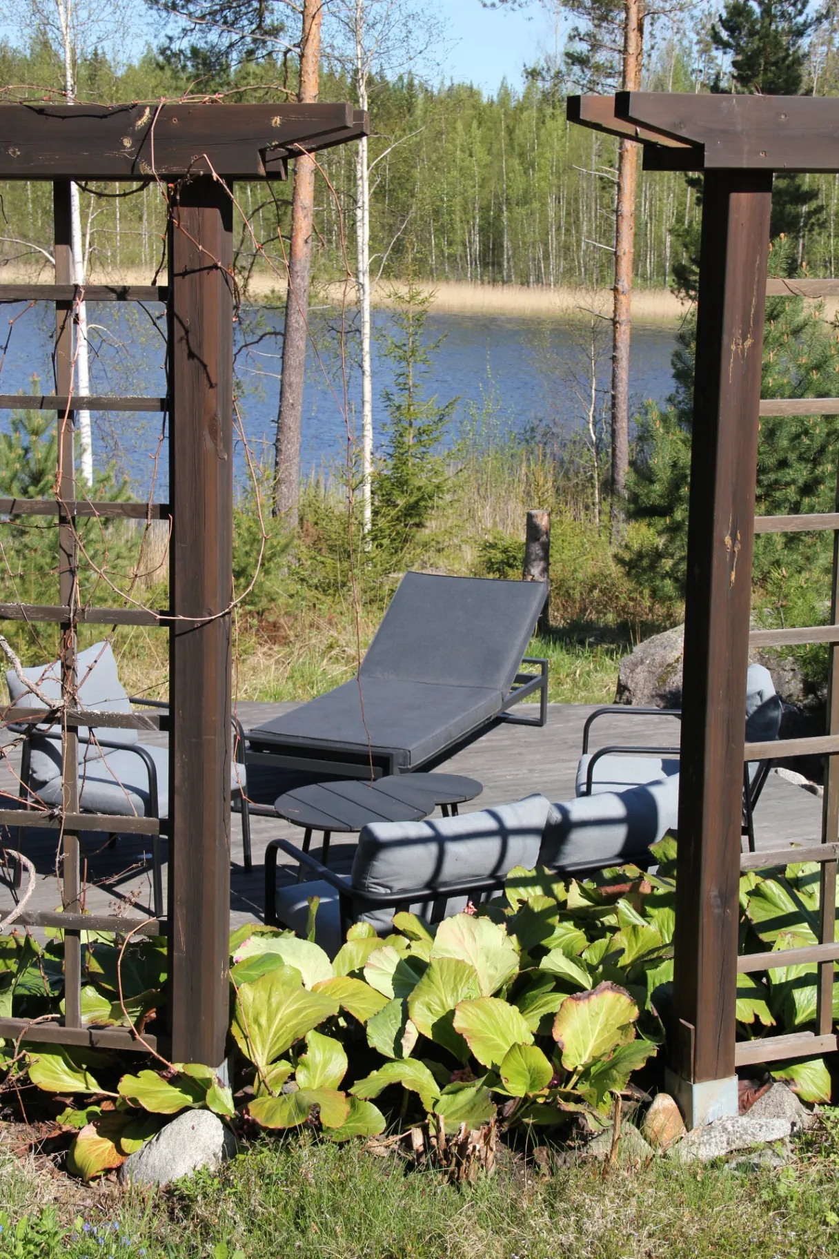 Lounger and armchairs framed by a wooden trellis at the water's edge