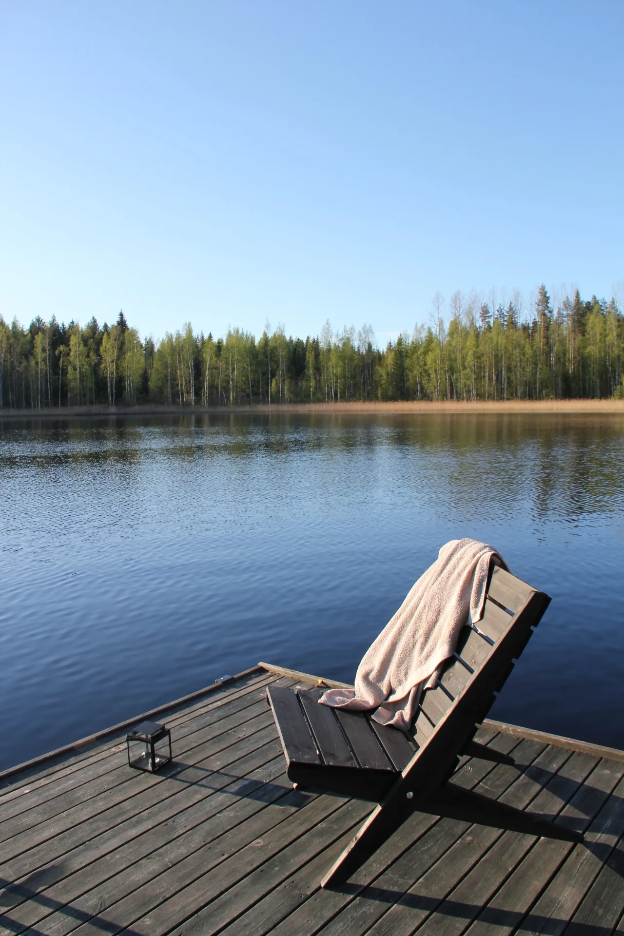 Lounge chair on the dock with calm lake and forest beyond